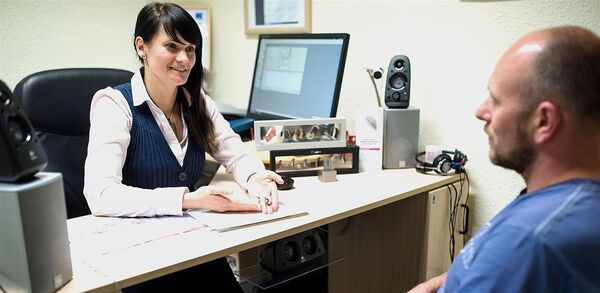 Eine Hörakustikerin berät einen Kunden in einem modernen Hörgeräte-Fachgeschäft.