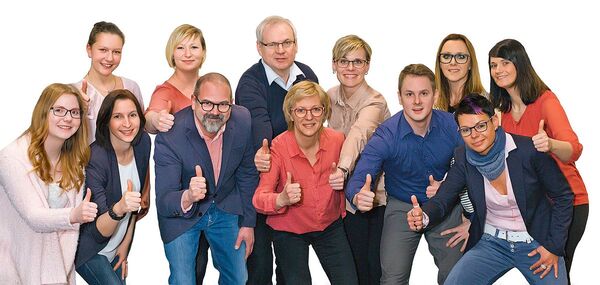 Teamfoto von Mitarbeitern eines Unternehmens, die gemeinsam lächelnd Daumen hoch zeigen.